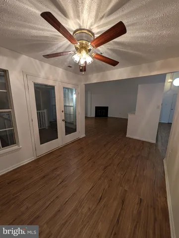 a view of an empty room with wooden floor and a ceiling fan