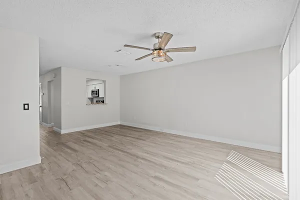 an empty room with wooden floor chandelier fan and windows