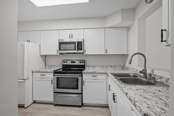 a kitchen with stainless steel appliances granite countertop a sink stove a refrigerator and white cabinets with wooden floor