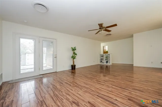 a view of empty room with wooden floor and fan