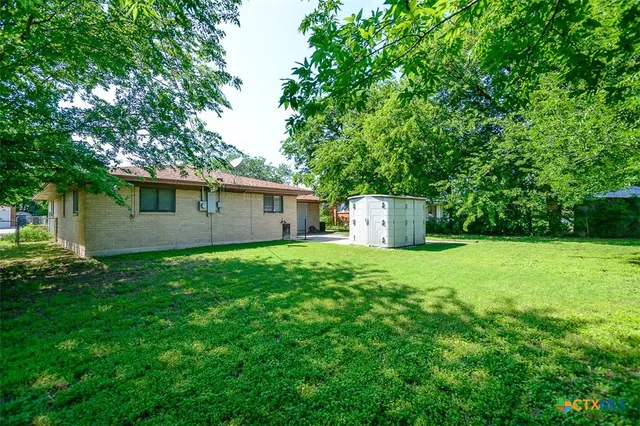 a backyard of a house with plants and large tree
