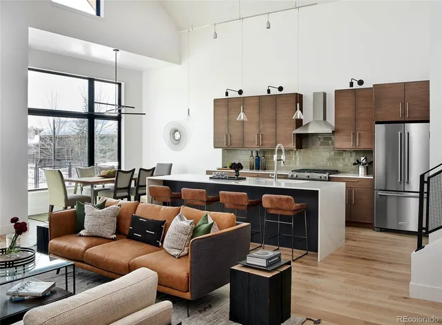 a living room with stainless steel appliances kitchen island granite countertop a refrigerator a stove and a wooden floor