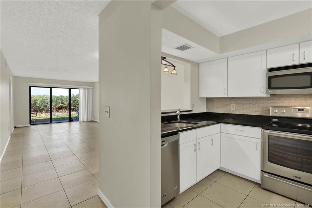 7400 South Ocean Drive, Unit 102 Jensen Beach, FL 34957 - Photo 6 of 26 a kitchen with stainless steel appliances granite countertop a stove a sink and white cabinets