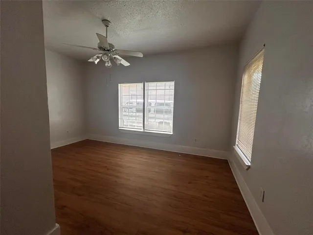 an empty room with wooden floor fan and windows