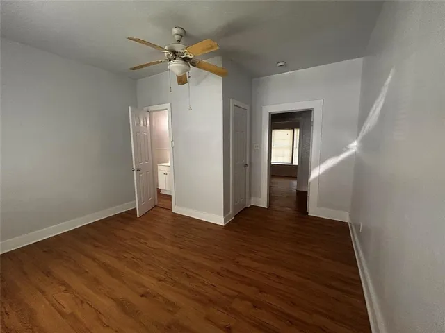 a view of an empty room with wooden floor and a ceiling fan