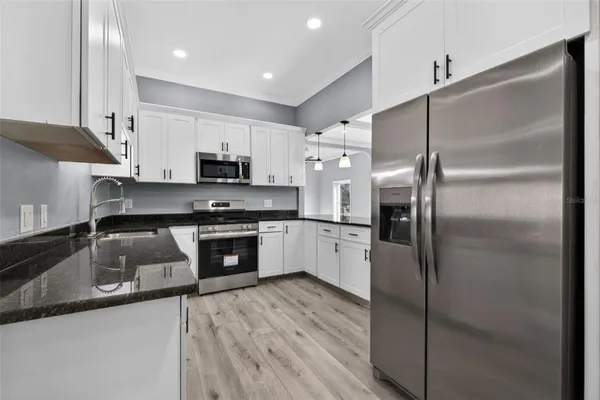 a kitchen with granite countertop a refrigerator a sink and white cabinets
