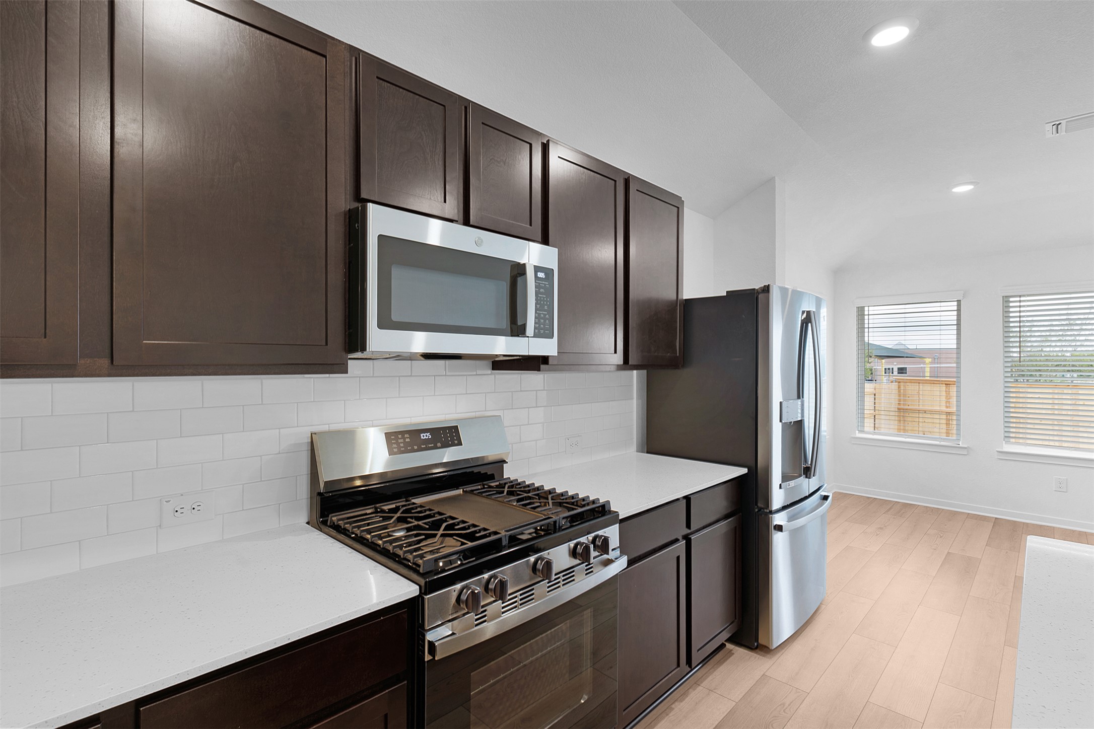 13721 Tucker Hedge Pass Elgin, TX 78621 - Photo 10 of 28 Kitchen with appliances with stainless steel finishes, dark brown cabinetry, lofted ceiling, decorative backsplash, and light wood-style floors