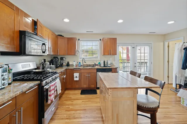 a kitchen with stainless steel appliances granite countertop a stove top oven a sink dishwasher a dining table and chairs with wooden floor