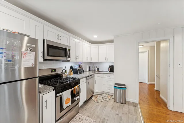 a kitchen with stainless steel appliances granite countertop a stove top oven a refrigerator a sink and white cabinets