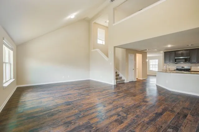 a view of an empty room and kitchen with wooden floor
