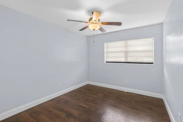 an empty room with wooden floor chandelier fan and windows
