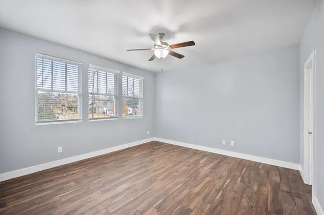 an empty room with wooden floor ceiling fan and windows