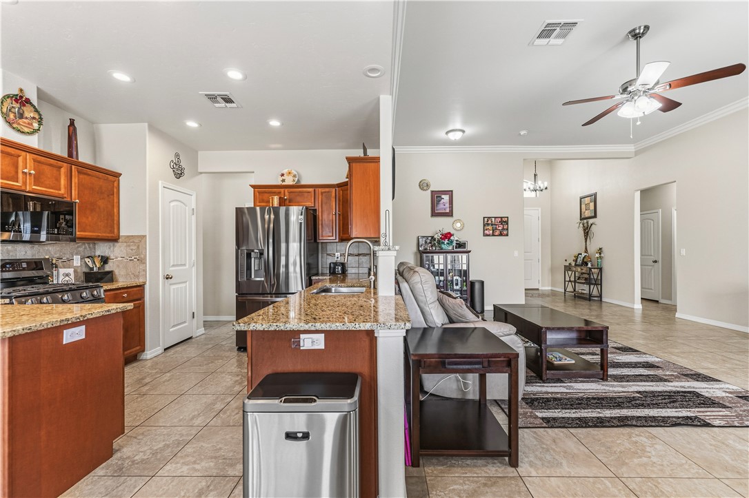4143 North Stampede Road Kingman, AZ 86401 - Photo 14 of 42 Open-concept living area with tile flooring throughout, featuring a kitchen with wood cabinetry and granite countertops, and a living room with crown molding and a ceiling fan