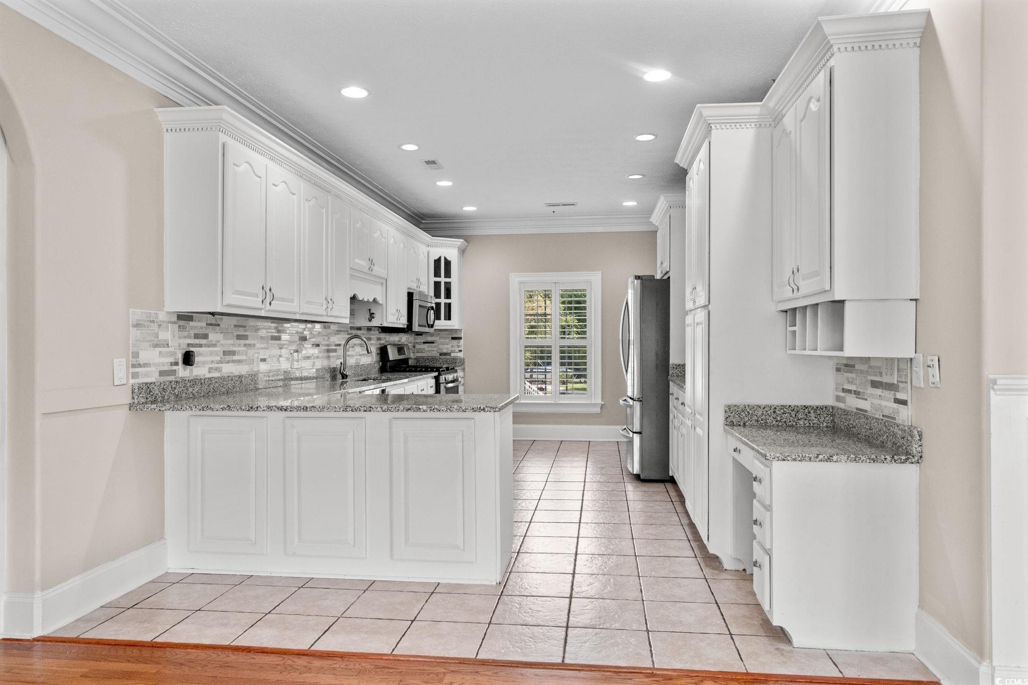 6912 Bay Road Myrtle Beach, SC 29588 - Photo 12 of 38 Kitchen featuring tasteful backsplash, a peninsula, ornamental molding, light tile patterned floors, and appliances with stainless steel finishes