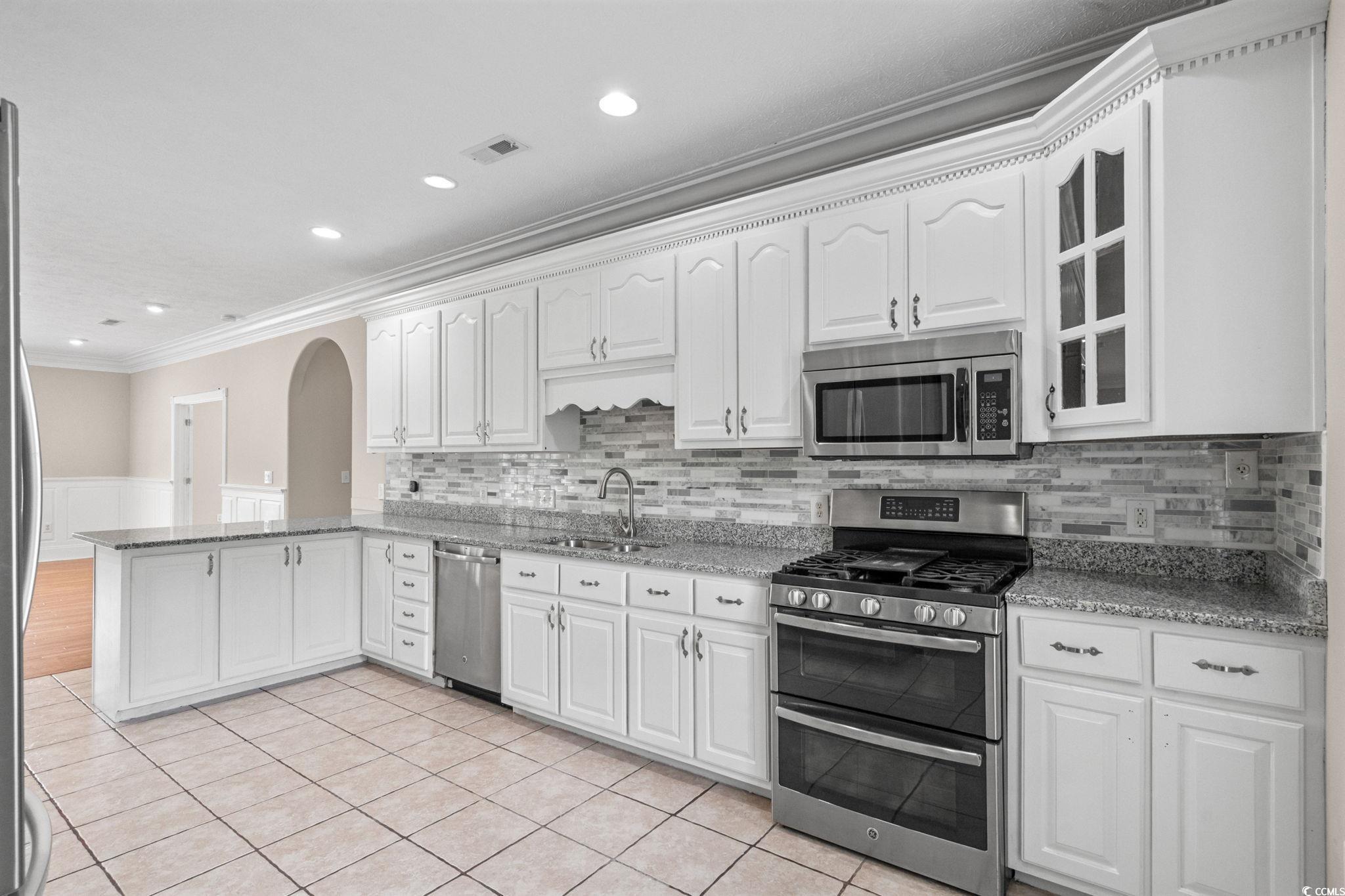 6912 Bay Road Myrtle Beach, SC 29588 - Photo 13 of 38 Kitchen featuring ornamental molding, stainless steel appliances, wainscoting, a peninsula, and arched walkways