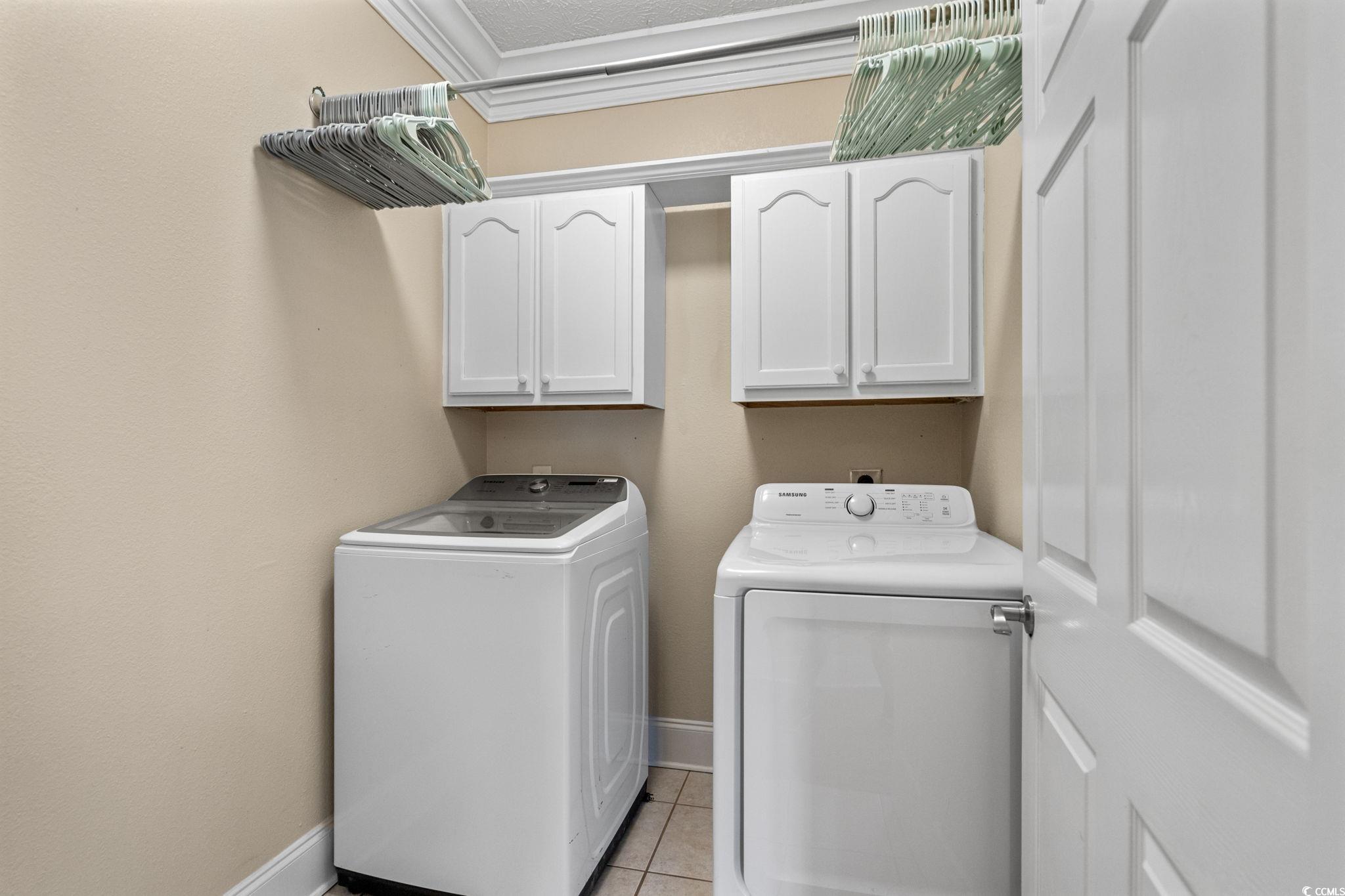 6912 Bay Road Myrtle Beach, SC 29588 - Photo 16 of 38 Laundry room with washer and clothes dryer, cabinet space, light tile patterned flooring, ornamental molding, and a textured ceiling