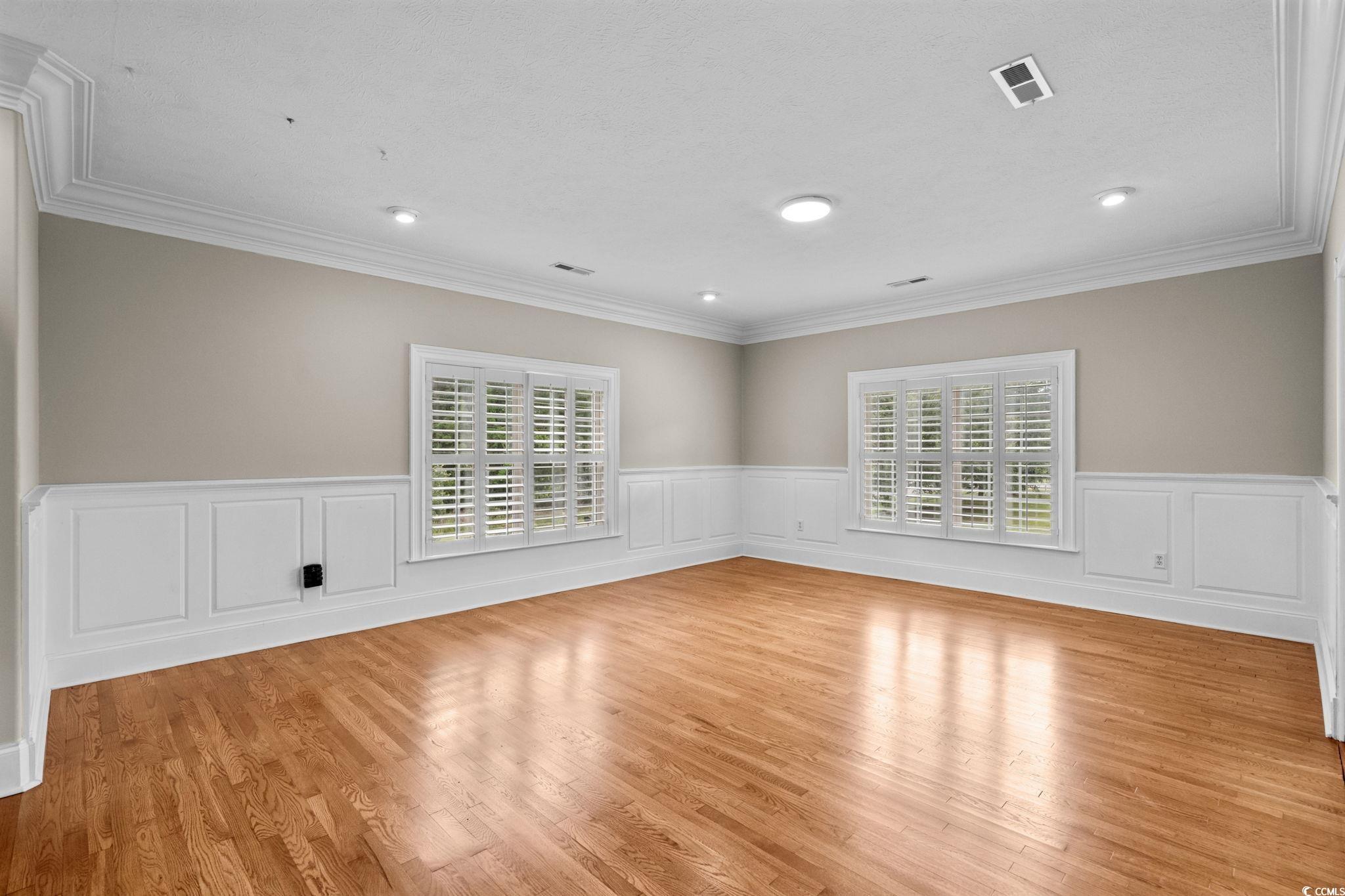 6912 Bay Road Myrtle Beach, SC 29588 - Photo 4 of 38 Empty room featuring plenty of natural light, wainscoting, a decorative wall, light wood finished floors, and crown molding
