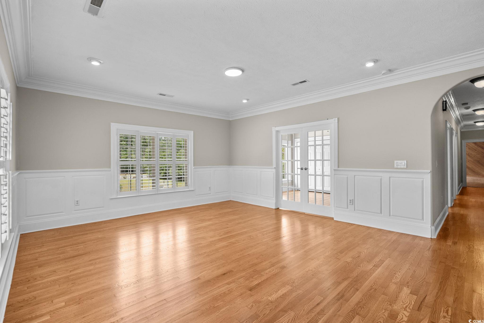 6912 Bay Road Myrtle Beach, SC 29588 - Photo 5 of 38 Empty room featuring arched walkways, a decorative wall, healthy amount of natural light, a wainscoted wall, and light wood-type flooring