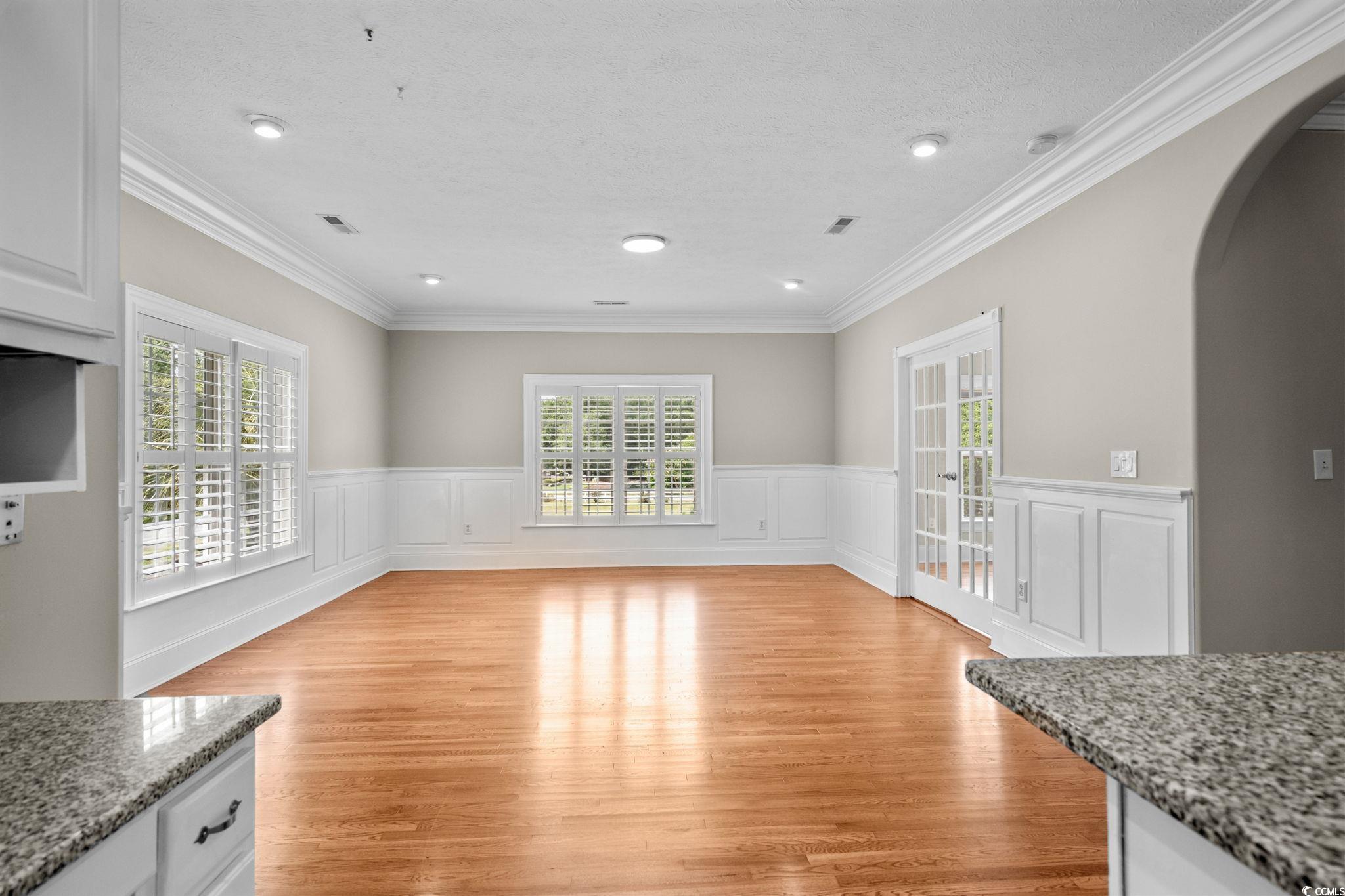 6912 Bay Road Myrtle Beach, SC 29588 - Photo 6 of 38 Unfurnished dining area with arched walkways, light wood-style flooring, a decorative wall, crown molding, and a wainscoted wall