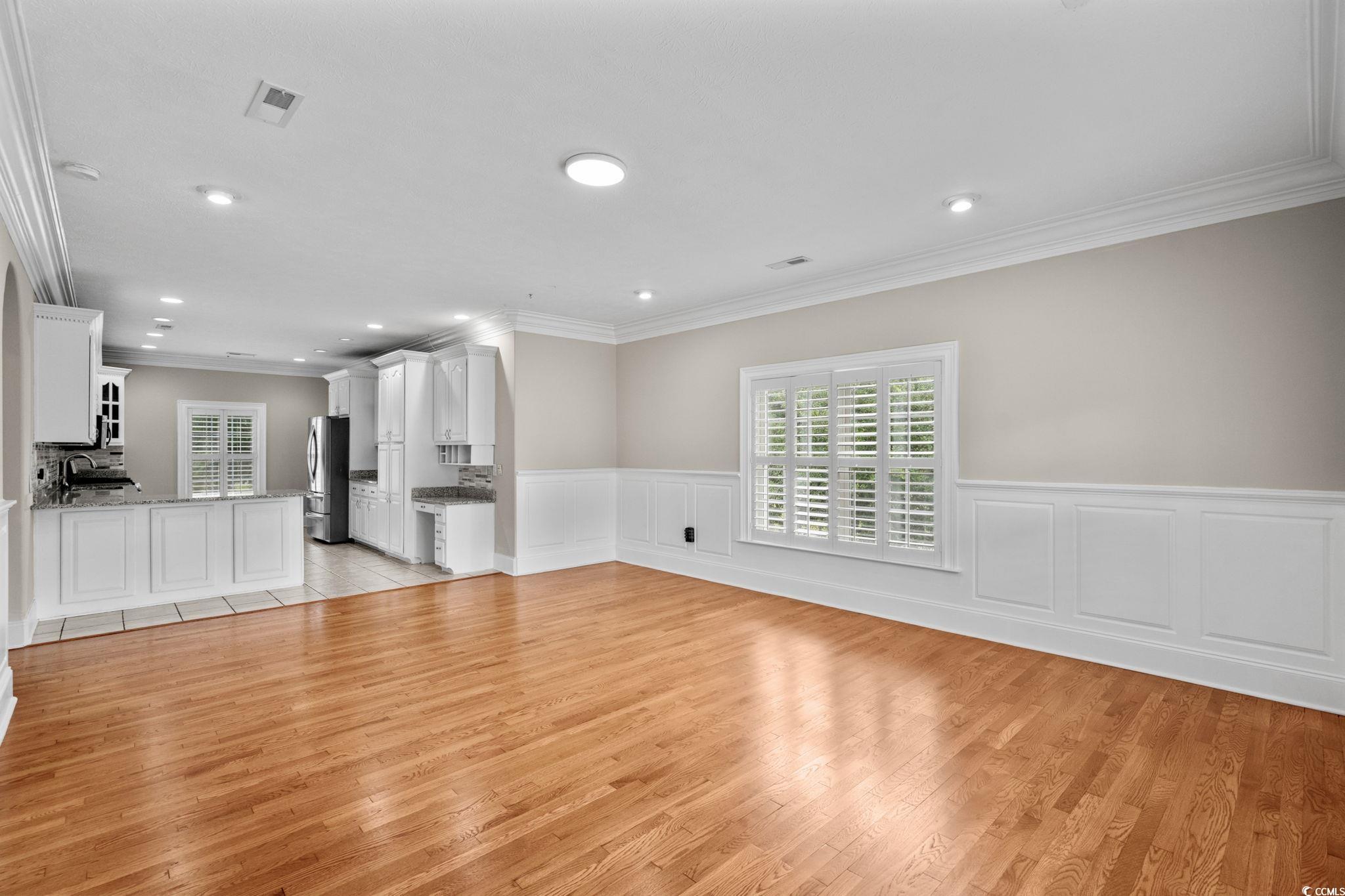 6912 Bay Road Myrtle Beach, SC 29588 - Photo 7 of 38 Unfurnished living room with healthy amount of natural light, a wainscoted wall, a decorative wall, crown molding, and light wood-style flooring