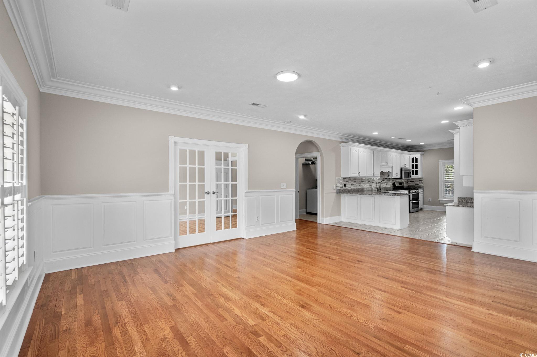 6912 Bay Road Myrtle Beach, SC 29588 - Photo 8 of 38 Unfurnished living room with a decorative wall, a wainscoted wall, arched walkways, crown molding, and light wood-style floors