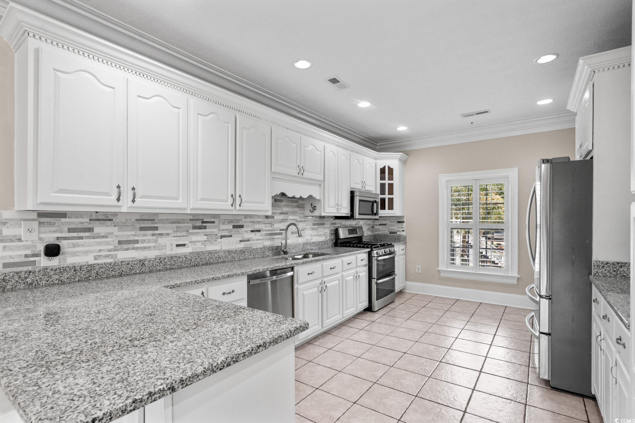 6912 Bay Road Myrtle Beach, SC 29588 - Photo 9 of 38 Kitchen with stainless steel appliances, white cabinetry, crown molding, decorative backsplash, and a peninsula