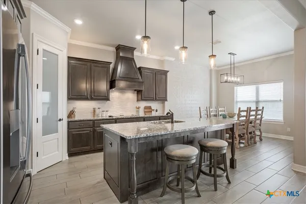 a kitchen with stainless steel appliances granite countertop a sink a stove a refrigerator and chairs
