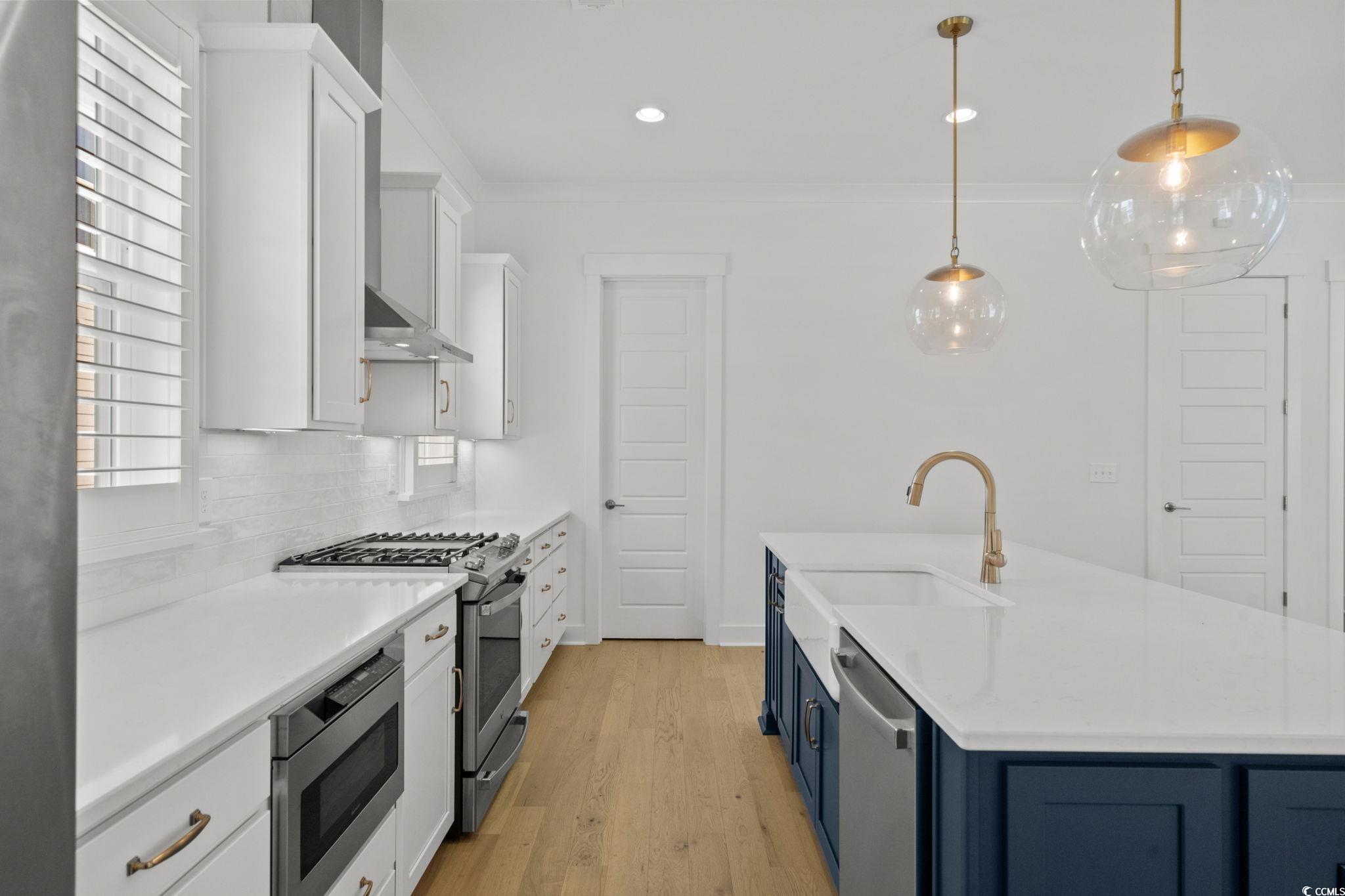 477 Ayrhill Loop Myrtle Beach, SC 29588 - Photo 13 of 39 Kitchen featuring white cabinets, blue cabinetry, appliances with stainless steel finishes, light wood finished floors, and hanging light fixtures