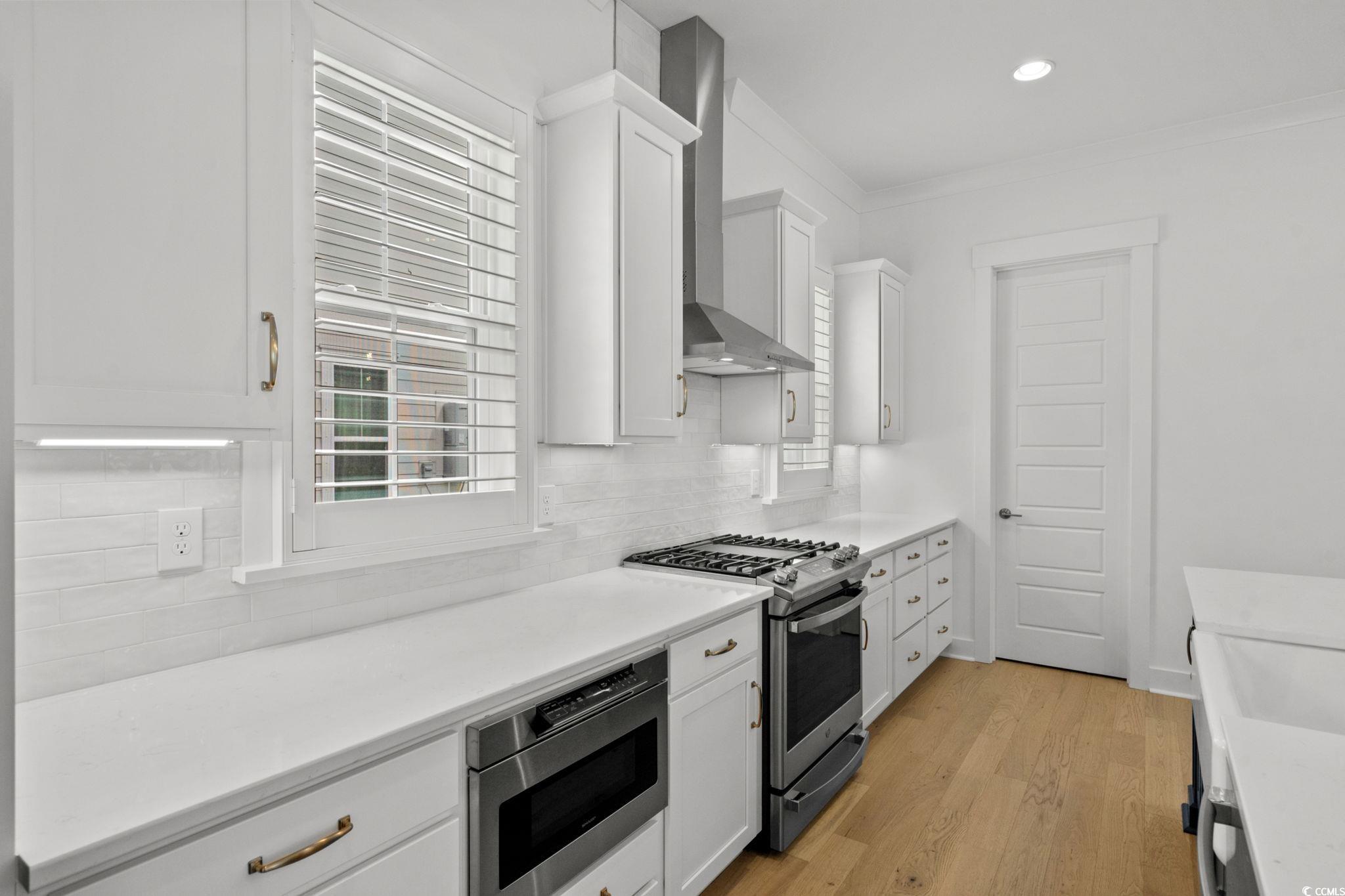 477 Ayrhill Loop Myrtle Beach, SC 29588 - Photo 14 of 39 Kitchen with white cabinets, appliances with stainless steel finishes, light wood-style floors, backsplash, and ornamental molding