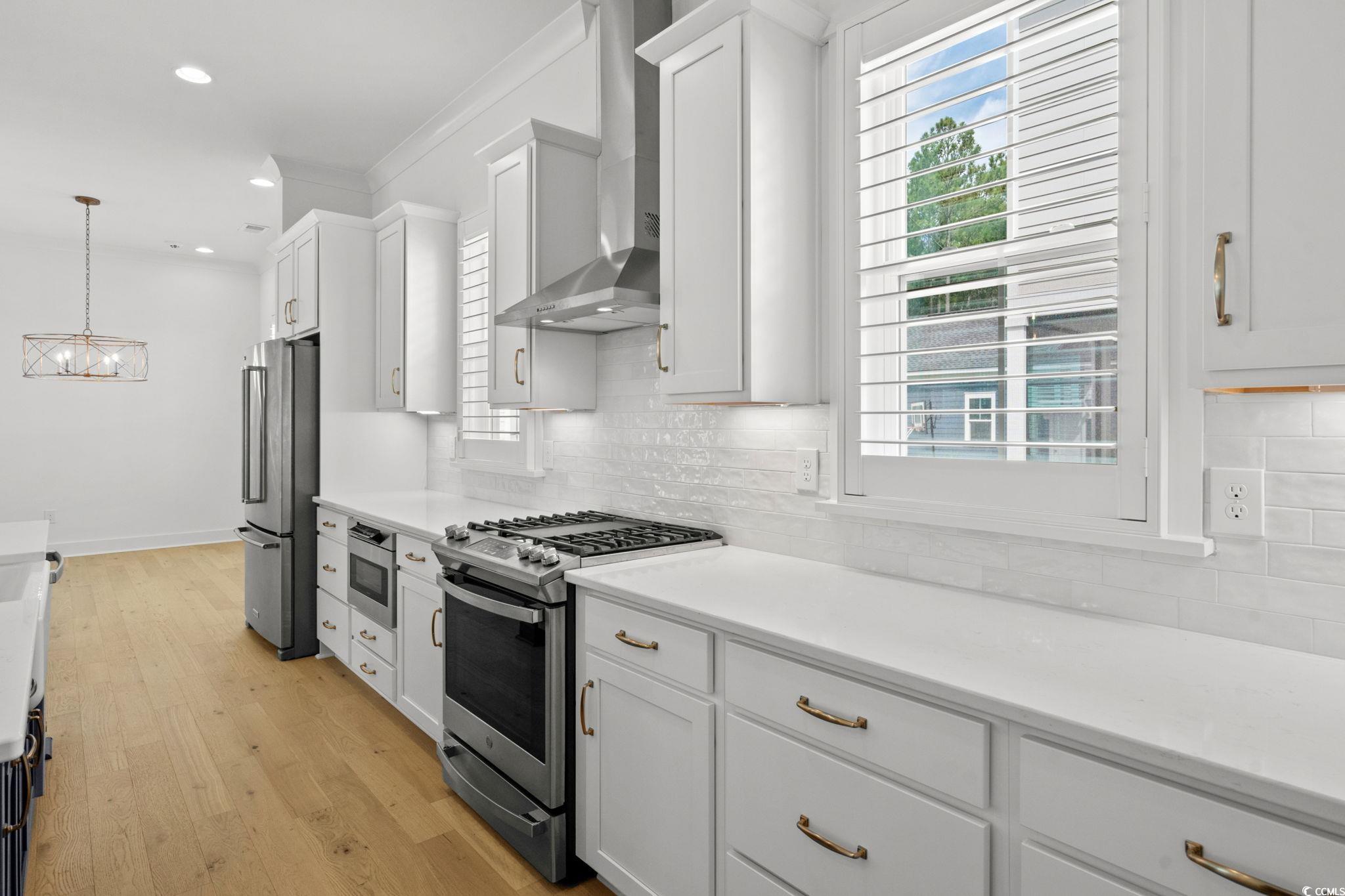 477 Ayrhill Loop Myrtle Beach, SC 29588 - Photo 15 of 39 Kitchen featuring appliances with stainless steel finishes, light wood-type flooring, pendant lighting, white cabinets, and crown molding