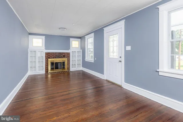 an empty room with wooden floor a fireplace and windows