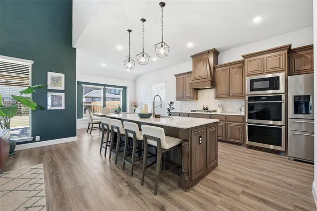 a open kitchen with stainless steel appliances granite countertop a stove a refrigerator a kitchen island a dining table and chairs with wooden floor