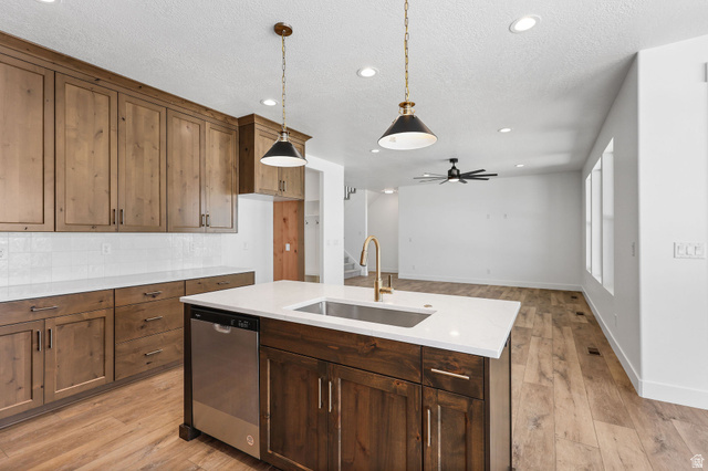 1144 South 4475 West West Point, UT 84015 - Photo 11 of 30 Kitchen featuring wood-finish cabinetry, a central island with a built-in sink, stainless steel dishwasher, and quartz countertops
