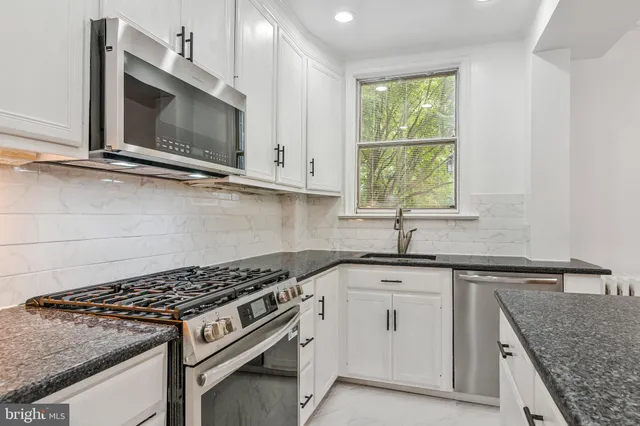a kitchen with granite countertop a sink stainless steel appliances and window