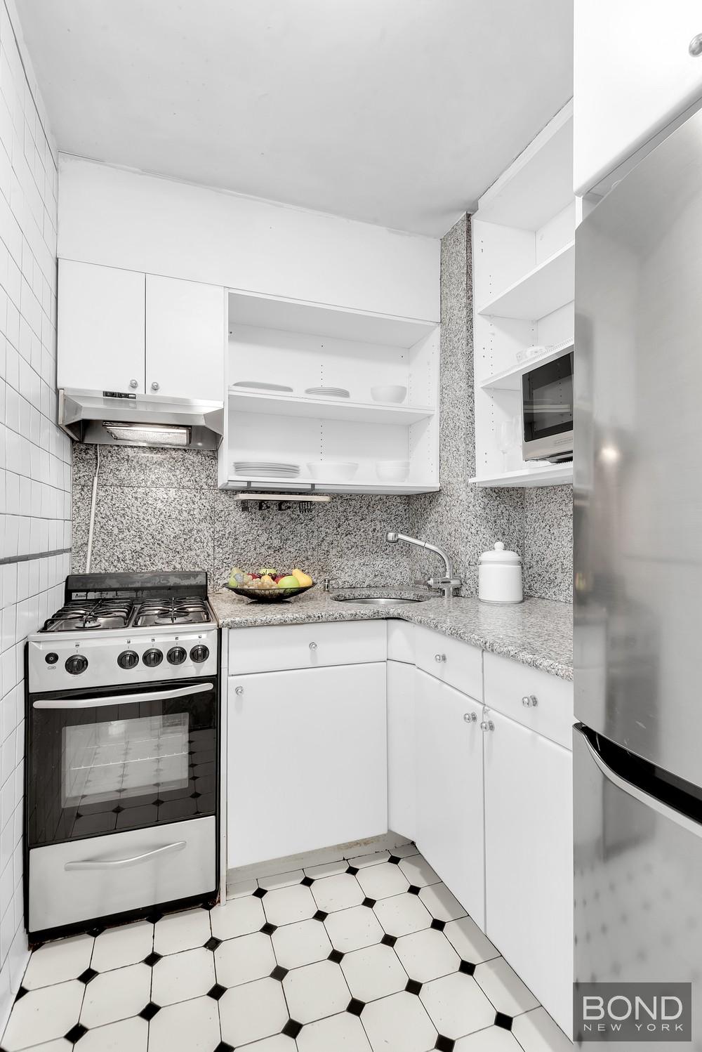 210 East 36th Street, Unit 5E Manhattan, NY 10016 - Photo 5 of 12 a kitchen with granite countertop a stove top oven microwave and cabinets