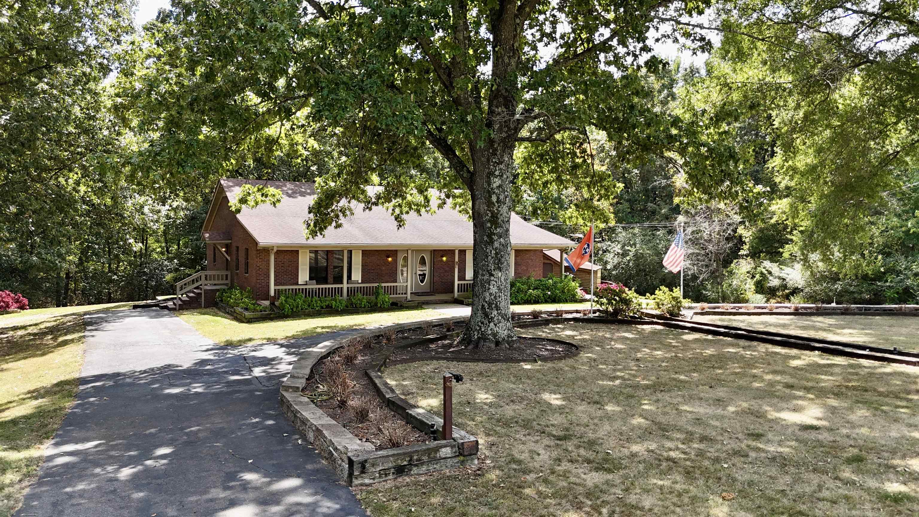420 Joann Road Somerville, TN 38068 - Photo 38 of 40 Brick exterior featuring a covered porch, mature trees, a paved driveway, and stone retaining walls