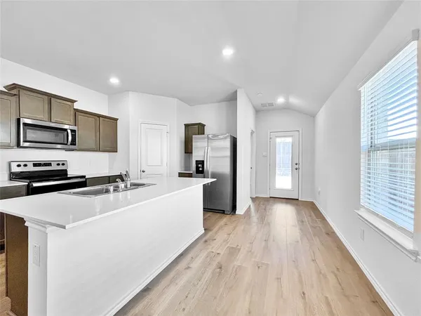 a large kitchen with a large counter top appliances a sink cabinets and a window