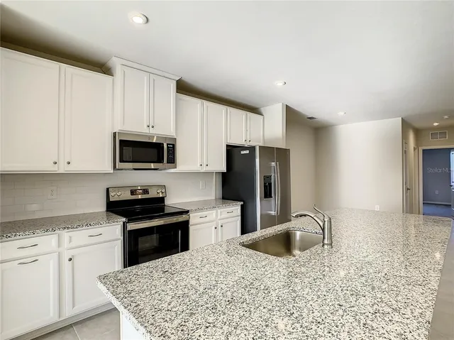 a kitchen with stainless steel appliances granite countertop a stove top oven a sink dishwasher and a refrigerator with wooden cabinets