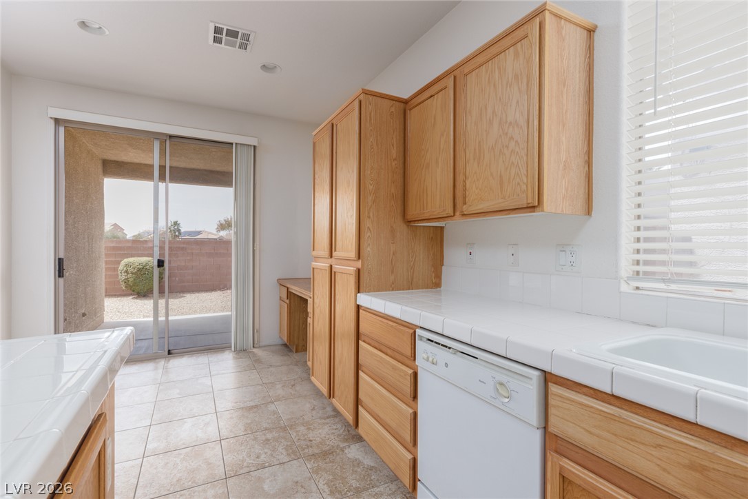 787 Rise Canyon Drive Henderson, NV 89052 - Photo 7 of 22 A well-lit kitchen with natural light oak cabinetry and practical tiled countertops.