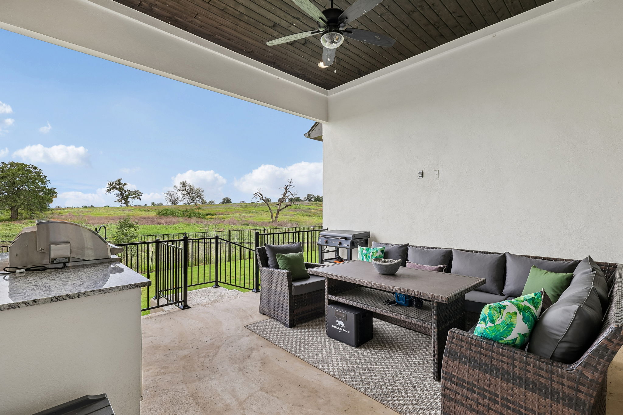 130 Firethorn Loop Bastrop, TX 78602 - Photo 27 of 38 Covered patio featuring a built-in outdoor kitchen with granite-look countertop, a ceiling fan, and a black metal fence overlooking expansive green space