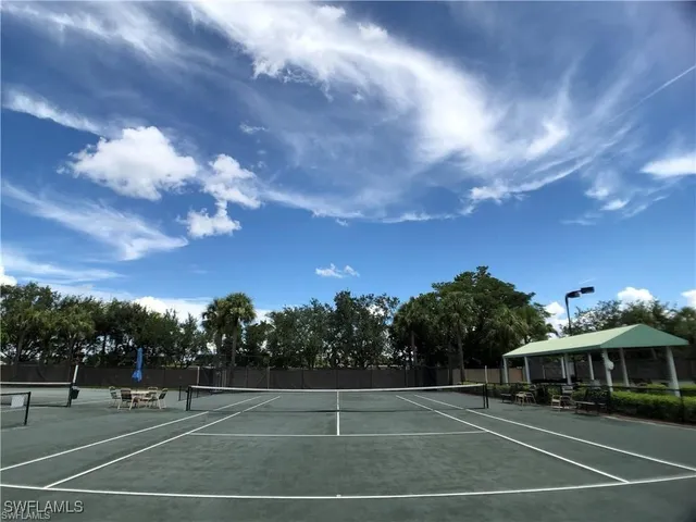 a view of a tennis ground with a table and chairs under an umbrella