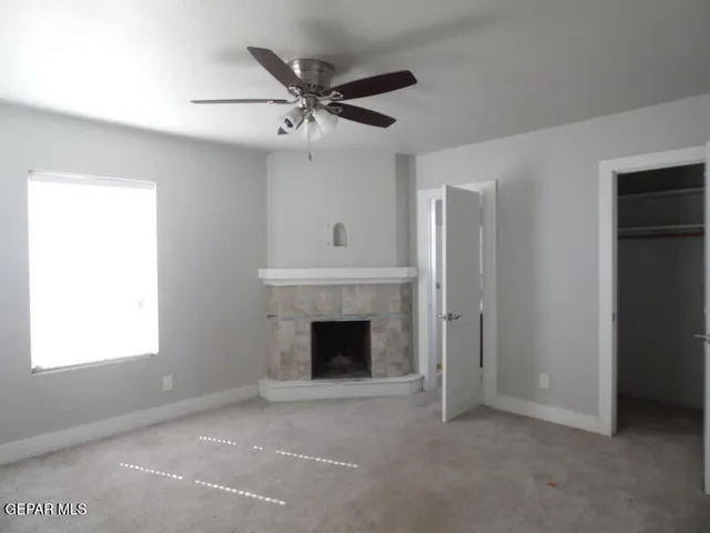 a view of an empty room with chandelier fan and fire place