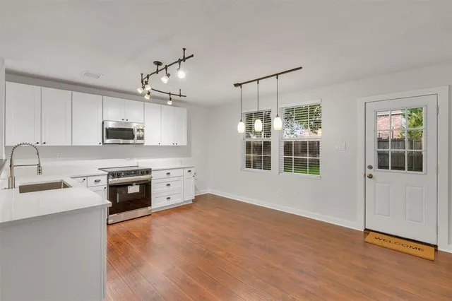 a kitchen with stainless steel appliances granite countertop a stove top oven a sink dishwasher a refrigerator and white cabinets with wooden floor