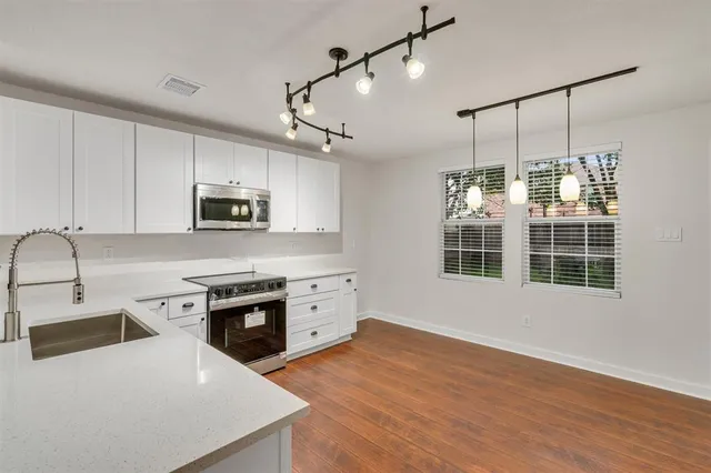 a kitchen with stainless steel appliances granite countertop a stove a sink a refrigerator and white cabinets with wooden floor