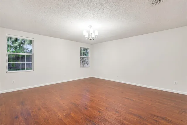 an empty room with wooden floor chandelier and windows