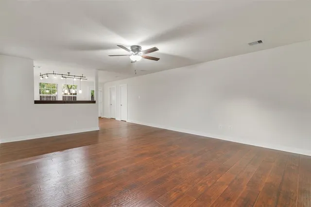 an empty room with wooden floor chandelier fan and windows
