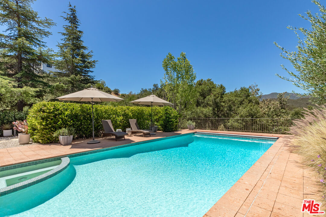 1045 Cold Canyon Road Calabasas, CA 91302 - Photo 21 of 51 a view of a swimming pool with a table and chairs under an umbrella