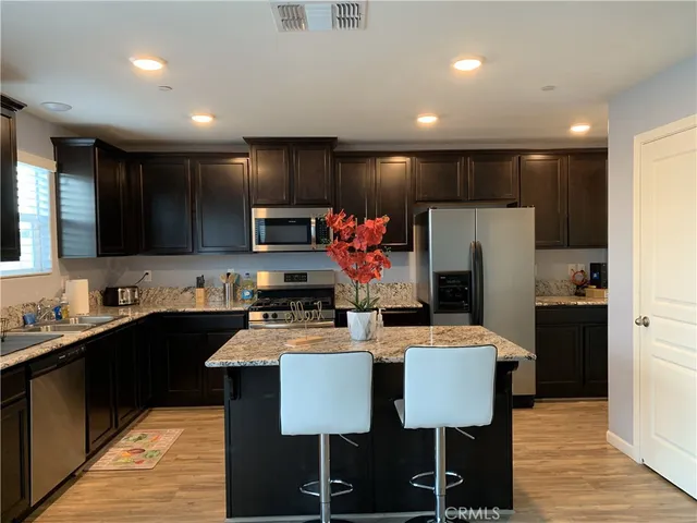 a kitchen with stainless steel appliances kitchen island granite countertop a table chairs sink refrigerator and microwave