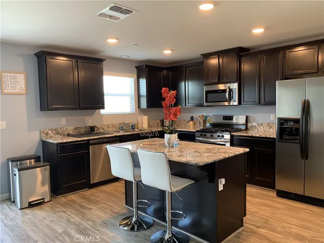 a kitchen with stainless steel appliances granite countertop a refrigerator a stove top oven a sink dishwasher and white cabinets with wooden floor