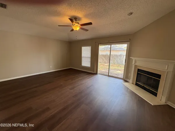 a view of an empty room with wooden floor fireplace and a window